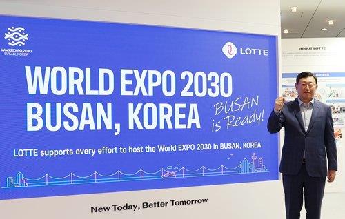 신동빈 회장이 부산 엑스포를 홍보하는 대형 스크린 앞에서 기념 촬영하는 모습.